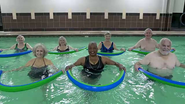 成熟的成年人在游泳池里用池面锻炼，看着镜头微笑。视频下载