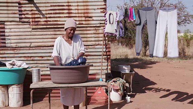 一个没有自来水的非洲妇女在她的铁皮小屋前用水桶洗衣服视频下载
