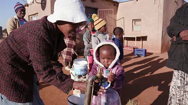 一个非洲小女孩从水龙头里取水，而南非严重干旱导致妇女和儿童排队用塑料容器取水视频素材