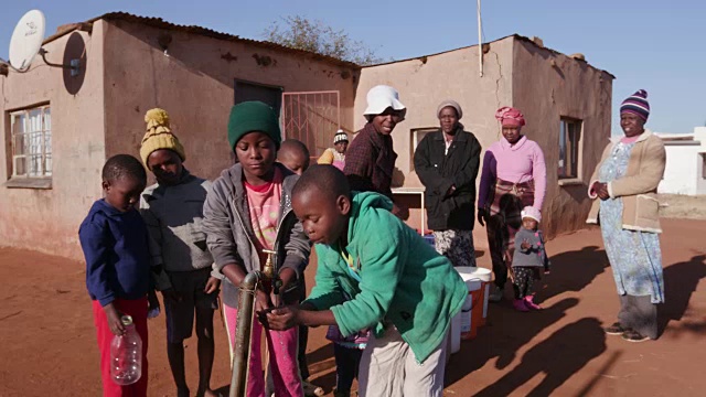 在南非，由于严重的干旱，年轻的非洲男孩从水龙头里喝水，而妇女在排队收集塑料容器里的水视频素材