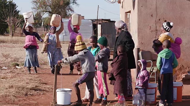 在南非，由于严重的干旱，年轻的非洲男孩从水龙头里喝水，而妇女在排队收集塑料容器里的水视频下载