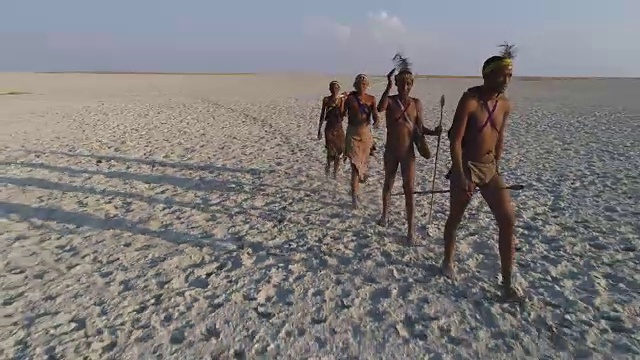镜头拉近，然后放大鸟瞰图，四名圣布须曼人正在穿越广阔的博茨瓦纳Makgadikgadi潘视频素材