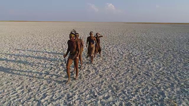这是四名圣布须曼人排成纵队，穿越广阔的博茨瓦纳Makgadikgadi pan的特写鸟瞰图视频素材