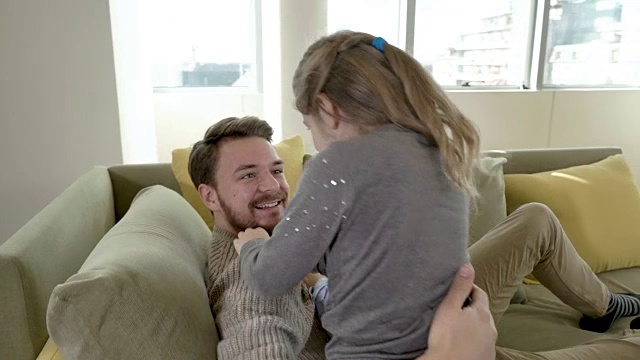 快乐的小男孩和小女孩拥抱在沙发上放松的父亲。视频素材