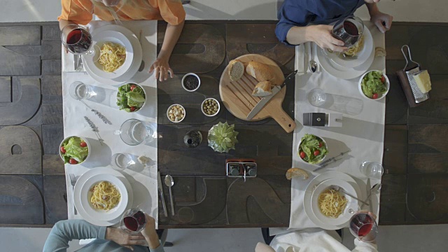 头顶顶视图表四个白种人朋友吃意大利干酪意面意大利面在午餐或晚餐，喝酒，干杯一起用红酒杯。夏季聚会在家里在现代的房子视频素材