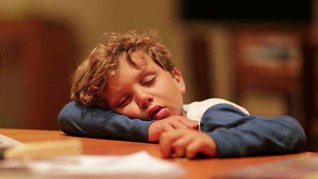 真实的孩子在一天的活动后疲惫的睡觉的时刻。小男孩耷拉着身子睡在桌子上，耗尽了精力，正在恢复体力视频素材