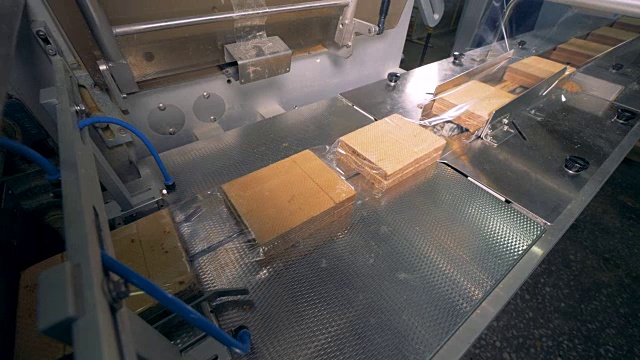 一长堆刚装进透明塑料膜的华夫饼正在传送带上移动。4 k。视频素材