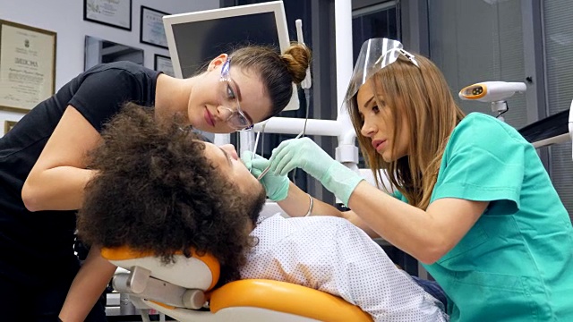 一名女牙医和她的助手给一名年轻男子检查牙齿的录像视频素材