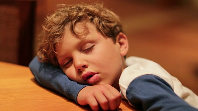 7岁的孩子流着口水在桌上睡着了。劳累了一天的小男孩在休息。生动、真实、真实的孩子睡觉的瞬间视频下载