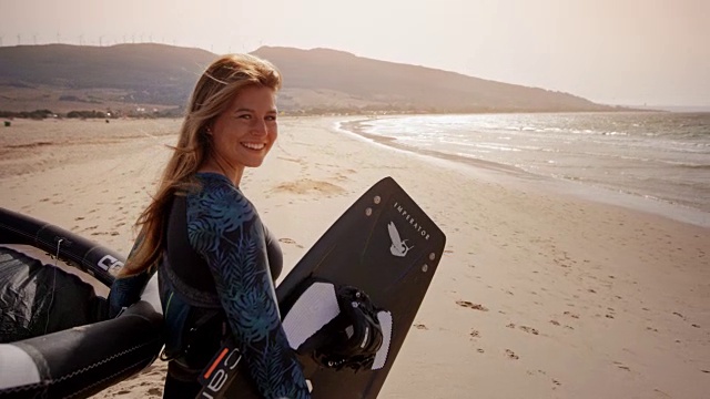 一个微笑的女性风筝的肖像站在阳光明媚的海滩上与她的装备视频素材