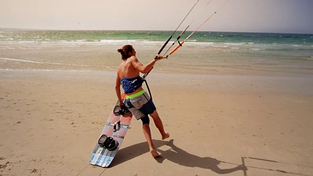 SLO MO Male风筝滑板手在海滩上捡起他的滑板，朝水里跑去视频素材