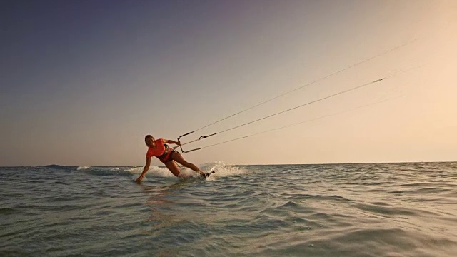 在日落时分，一个女人骑着她的风筝板，一只手在水里，对着镜头微笑视频下载