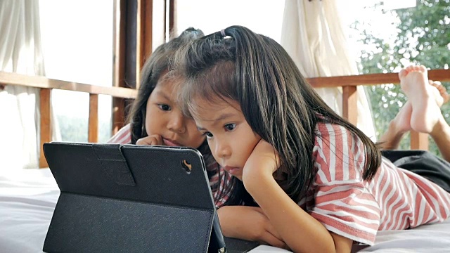 小女孩们在床上看平板电脑。慢动作拍摄在光的自然视频下载