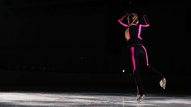 一名专业的滑冰运动员在冰上的空中旋转着表演跳跃动作。小女孩参加花样滑冰比赛视频素材