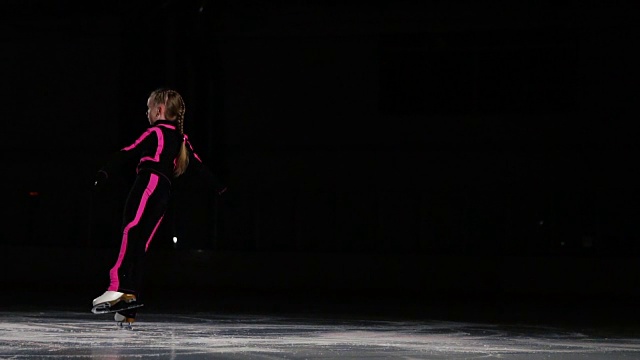 一名专业的滑冰运动员在冰上的空中旋转着表演跳跃动作。小女孩参加花样滑冰比赛。在黑暗背景下的一般轮廓视频素材