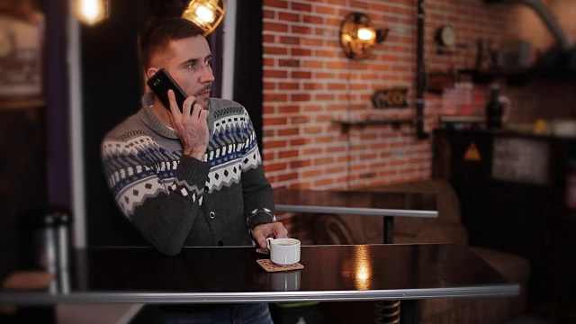 肖像年轻快乐有吸引力的男子坐在咖啡馆使用电话。一个拿着智能手机坐在酒吧里的帅哥视频素材
