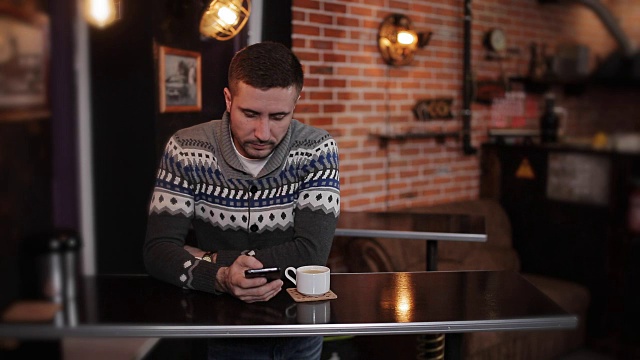 肖像年轻快乐有吸引力的男子坐在咖啡馆使用电话。一个拿着智能手机坐在酒吧里的帅哥视频素材