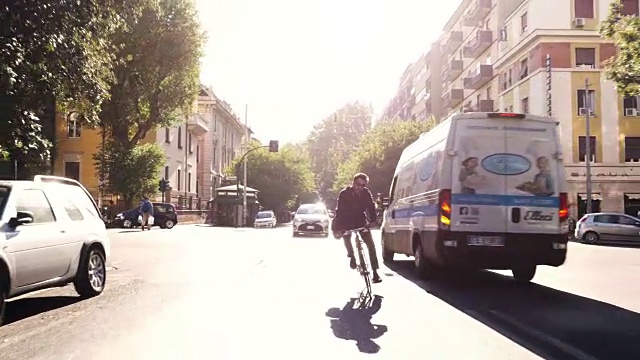 在阳光明媚的日子里，年轻的潮男骑着自行车在罗马市中心一条有树的道路上，戴着墨镜视频下载