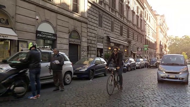在阳光明媚的日子里，一名年轻的潮男骑着自行车在罗马市中心的历史建筑旁行走，他还戴着墨镜视频素材