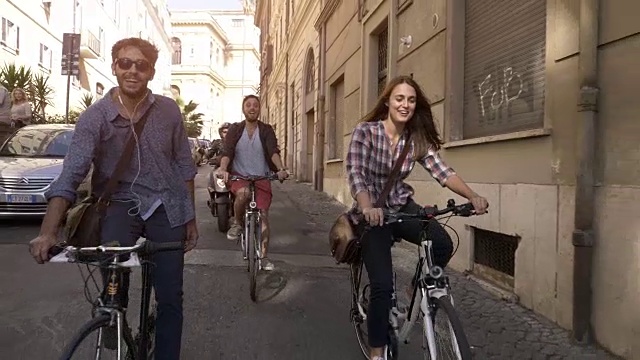 三个年轻的朋友游客在罗马市中心的小街道上骑自行车在阳光明媚的一天慢镜头汽车稳定摄影机视频下载