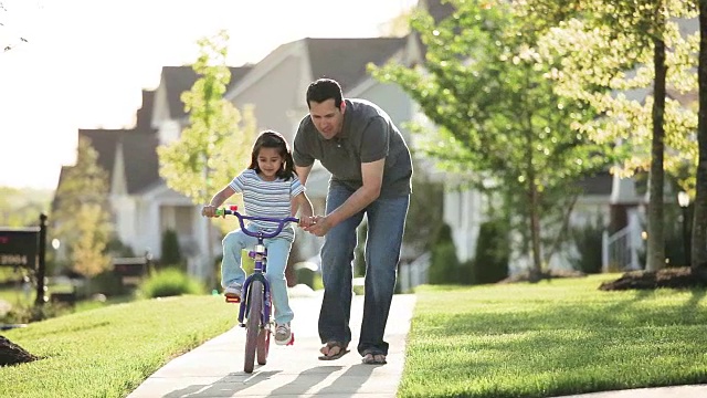 父亲教女儿在附近的人行道上骑自行车视频素材