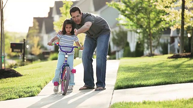 父亲教女儿在附近的人行道上骑自行车视频素材