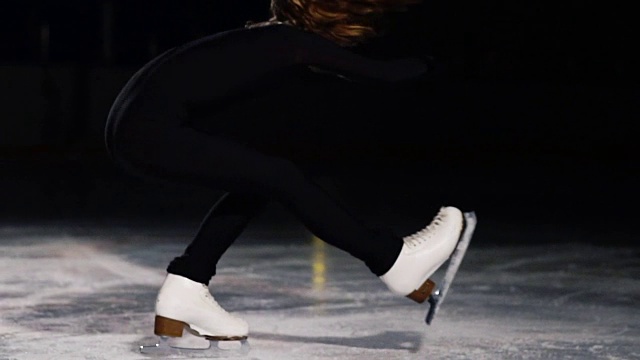 一个女孩在冰上滑冰的特写镜头进行了一个旋转，围绕她的轴，而站在冰上在冰上单腿在一个燕子的姿势。蹲到手枪的位置，并继续旋转视频素材