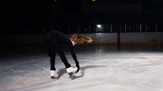 特写的一个女孩滑冰在冰上执行旋转围绕她的轴，而站在冰鞋上单腿。摄像机在绕着花样滑冰运动员的轨道上以慢动作移动视频素材