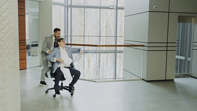 两个疯狂的商人坐在办公椅上，把文件扔起来，在现代商业中心的大厅里玩的慢动作视频下载