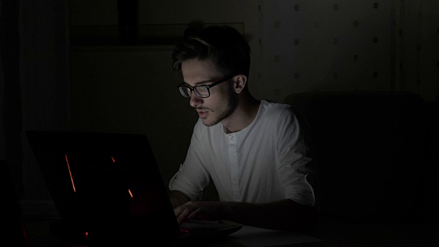一名年轻困惑的学生深夜在家里一边用笔记本电脑一边擦拭眼镜视频下载