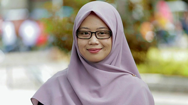 一幅美丽的东南亚穆斯林妇女戴着头巾在公园里用三种色调在镜头前微笑的肖像视频下载