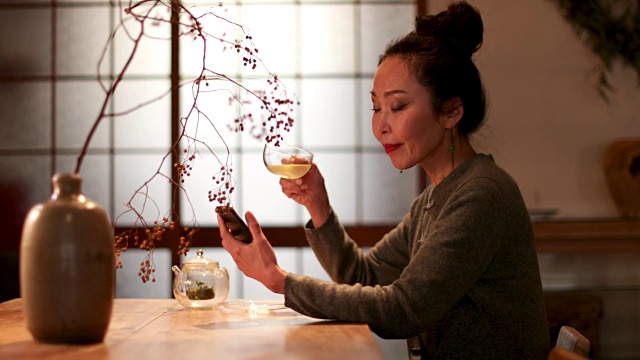 日本女性在传统的房子里喝绿茶，看手机短信视频下载