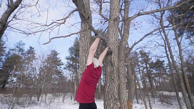 强壮的运动的年轻人正在拔一根树枝在一个冬天的公园在白天，举腿视频素材