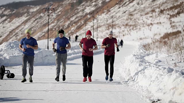 在寒冷的冬日里，四名运动员穿着运动服，戴着帽子，在雪道上慢跑视频素材