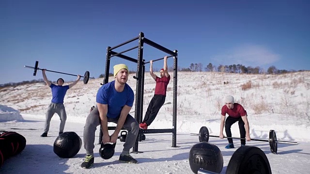 冬日里，四名青年运动员在操场上训练，一个在拉梁，一个在举壶铃，两个在举杆子视频素材