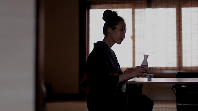 日本京都，日本妇女穿着和服在传统的窗口喝Saki视频素材