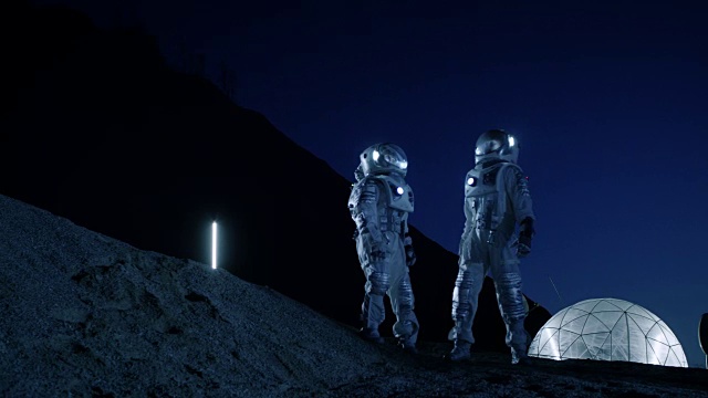两名宇航员穿着太空服站在外星看天空。在背景基地与球型圆顶。其他世界殖民和太空旅行的概念。视频素材
