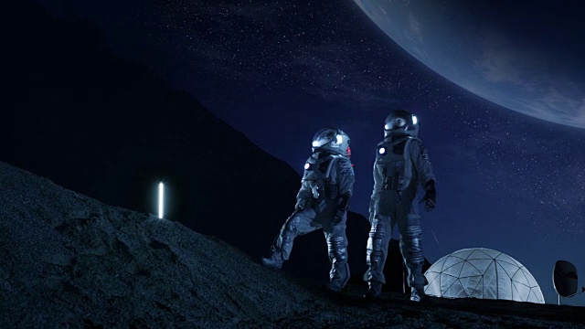 两名宇航员穿着太空服站在月球上看美丽的地球。在背景月球基地与测量圆顶。月球殖民和太空旅行概念。视频下载