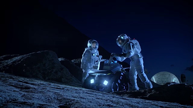 两名宇航员穿着宇航服在外星球上为表面探索任务准备太空车。关于太空殖民的未来概念。视频素材