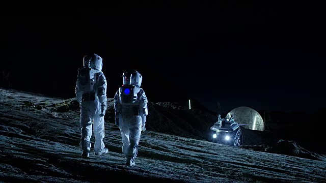 两名宇航员穿着宇航服在外星球上行走看着天空。在背景基地与球型圆顶。其他世界殖民和太空旅行的概念。视频下载