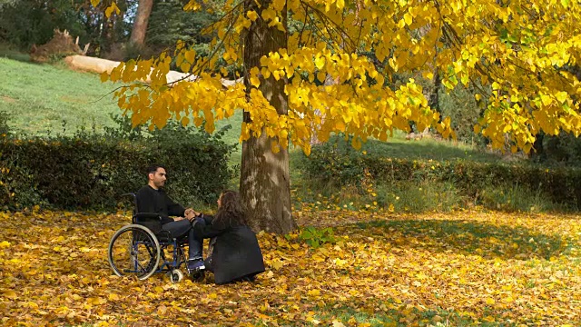 一个坐轮椅的男人和他的女朋友在秋天的公园里视频素材