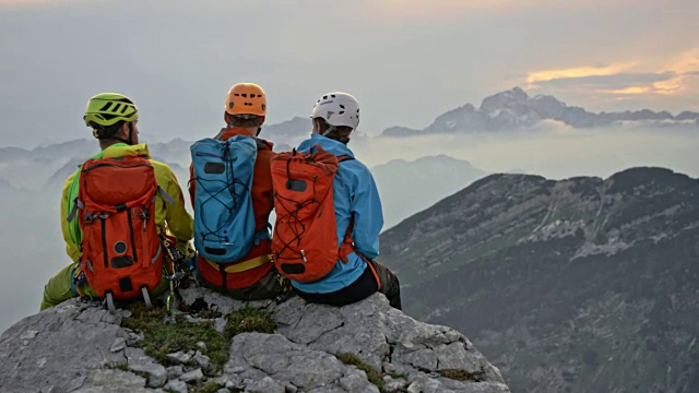 三个登山者坐在山顶的边缘聊天视频素材