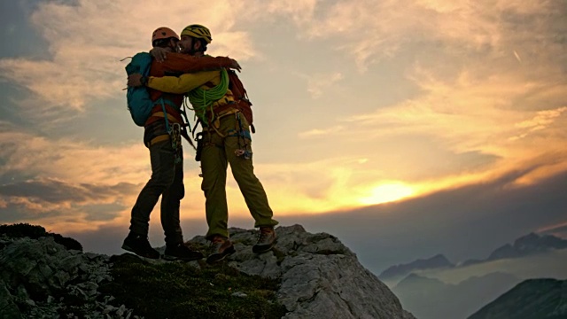 一位男性登山运动员在日落时分伸出手，帮助他的朋友到达山顶视频素材