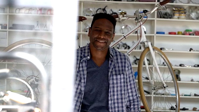 英俊的黑人自行车店老板看着镜头，双臂交叉微笑视频下载