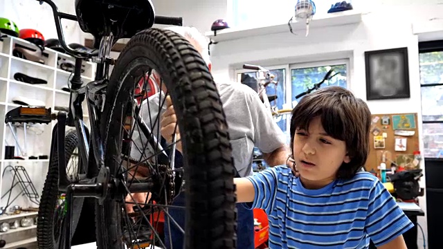 孙子正在调整他自行车后轮上的螺丝，爷爷教他视频素材