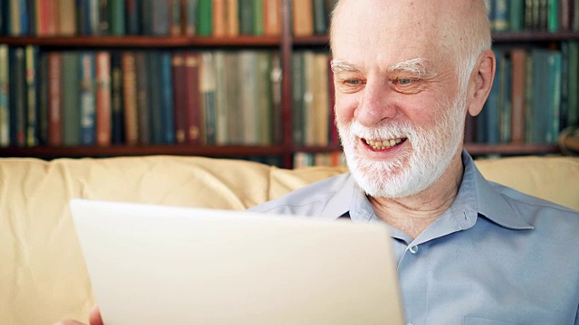 英俊的老年人在家里用笔记本电脑工作。收到好消息又兴奋又高兴视频素材