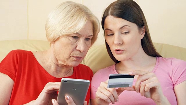 母女俩用智能手机上的信用卡在网上购物。老年人使用的技术视频素材