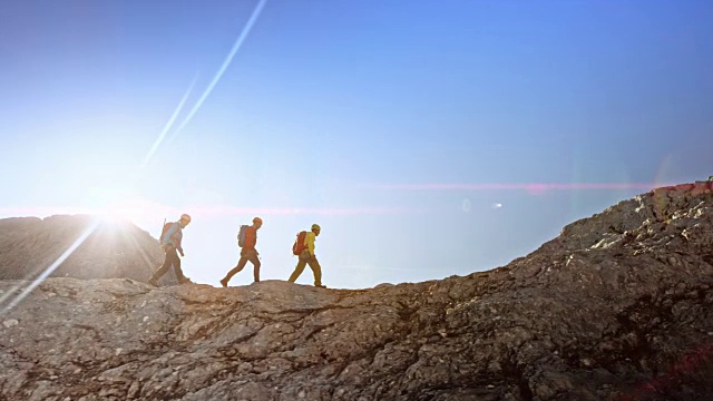 三个登山运动员在阳光下行走在岩石山脊上视频下载