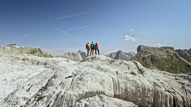 在一个阳光明媚的日子里，三个登山运动员在高山的岩石地形上行走视频下载