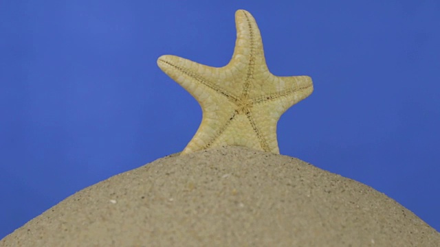 旋转着，黄色美丽的海星站在一堆沙子上。孤立的,蓝色屏幕视频素材